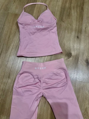 Rosa leggings och topp från GTECH - Säljer ett matchande set med ljusrosa leggings och topp från GTECH. Leggingsen har hög midja och sömlös design, medan toppen har smala axelband och en snygg passform. Materialet är stretchigt och mjukt, perfekt för träning eller chill.