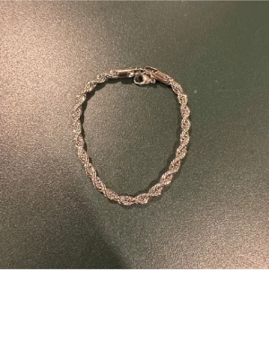 Silverfärgat tvinnat armband - Snyggt armband i silverfärg med tvinnad design. Armbandet har en klassisk karbinhake och passar perfekt för att ge din stil lite extra glans. Enkel men ändå iögonfallande detalj till din outfit.