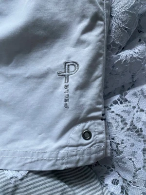 Vita shorts från Pelle P med brodyr - Snygga vita shorts från Pelle P med broderad logga framtill. Klassisk design med fickor och knappdetalj. Perfekta för varma dagar och lätta att matcha med olika toppar. Gjorda i bomull för en skön känsla.