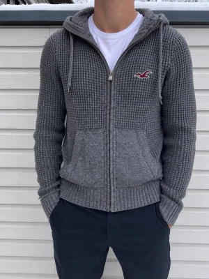 Hollister Grå Stickad Hoodie - Snygg och stilren grå stickad hoodie från Hollister. 🩶 Bra skick och riktigt snygg passform. Perfekt till hösten/vintern och enkel att matcha med jeans eller chinos.  📦 Skickas snabbt och packas noggrant!