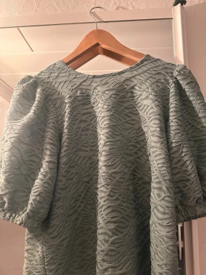 Grön strukturerad blus med puffärm - Snygg ljusgrön blus med puffiga korta ärmar och ett vågigt strukturerat tyg. Blusen har rund halsringning och en unik textur som ger ett trendigt intryck. Perfekt för dig som vill sticka ut lite extra.