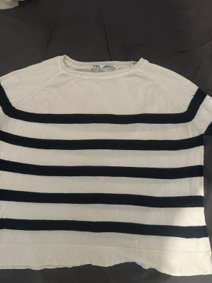 Vit och svart randig tröja från Zara - Snygg vit tröja från Zara med svarta horisontella ränder. Tröjan har rund halsringning, långa ärmar och ribbade muddar vid ärmslut och nederkant. Perfekt för en stilren och avslappnad look.
