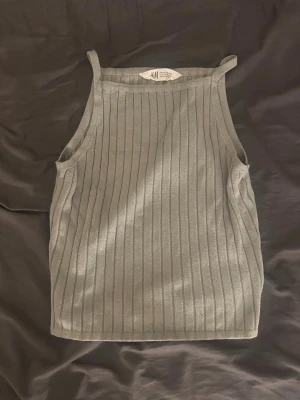 Grå ribbad linnetopp från H&M - Snygg grå ribbad linnetopp från H&M med raka axelband och smickrande passform. Toppen är ärmlös och har ett stilrent, randigt mönster som ger en modern vibe. Perfekt att matcha med jeans eller kjol för en trendig look. Är i storlek 146/152 men passar XS.