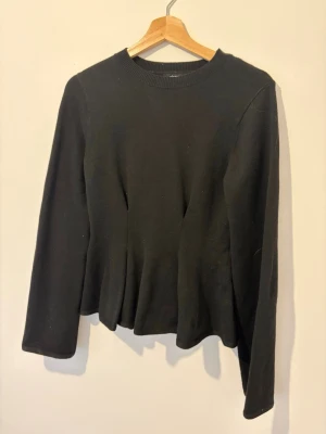 Svart långärmad tröja - En enkel svart långärmad tröja med rund halsringning och rak passform. Tröjan har ribbad kant vid halsen och är tillverkad i ett mjukt material som passar perfekt till olika outfits.
