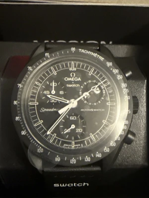 Omega x Swatch MoonSwatch svart klocka - Säljer en Omega x Swatch MoonSwatch Mission to the Moonphase. Klockan är svart med vit text och detaljer, har kronograf och tachymeter på boetten. Tillverkad i biokeramik och kommer i originalförpackning. Perfekt för dig som gillar stilrena accessoarer.