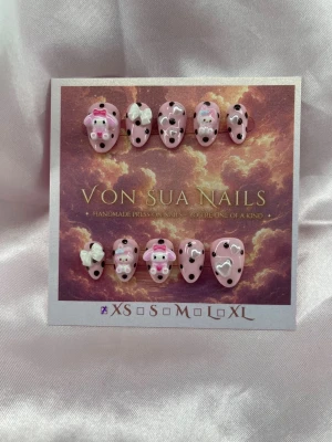 MelodyDots (XS);ExtraShortAlmond  - Set handgjorda press-on naglar i rosa med svart prickar , dekorerade med 3D-Charms som hjärtan, rosetter och söta My Melody figurer. Naglarna har en extra kort mandelform och är perfekta för dig som vill ha en unik och lekfull look.XS: 14 mm, 11 mm, 11,5 mm, 10 mm, 8 mm