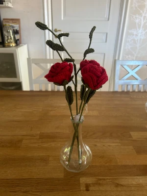 Virkade rosor i vas - Unika handgjorda virkade rosor i rött garn med gröna stjälkar och blad. Blommorna står i en enkel, genomskinlig glasvas. Perfekt som dekoration till hemmet eller som present till någon speciell.