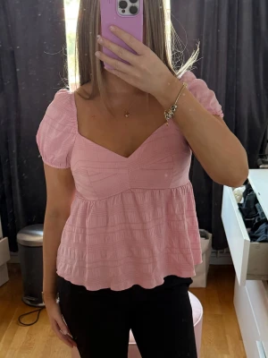 Ljusrosa puffärmad blus - Supersöt ljusrosa blus med puffärmar. Toppen har en luftig, lös passform och är sydd i ett mjukt, strukturerat bomullstyg. 