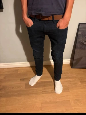 Mörkblå slim fit anbass jeans från Replay - Säljer ett par mörkblå slim fit jeans från Replay med klassisk femficksdesign och dragkedjedetalj på fickan. Jeansen har smal passform och är tillverkade i stretchigt denimtyg för extra komfort. Perfekta för en trendig och avslappnad look. 