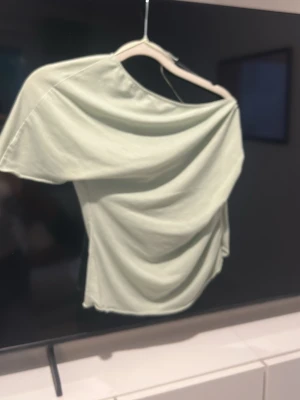 Ljusgrön offshoulder topp - Trendig ljusgrön topp med offshoulder-design och korta ärmar. Tillverkad i mjukt bomullsmaterial som ger en avslappnad och snygg look. Perfekt för dig som vill ha en enkel men ändå unik topp till garderoben.