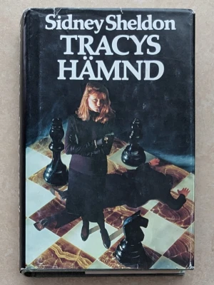Tracys hämnd av Sidney Sheldon - En spännande roman med svart hård pärm och omslag i mörka färger. Omslaget visar en kvinna på ett schackbräde med stora schackpjäser och dramatisk skugga. Boken är på svenska och har tydlig titel och författarnamn i vitt.