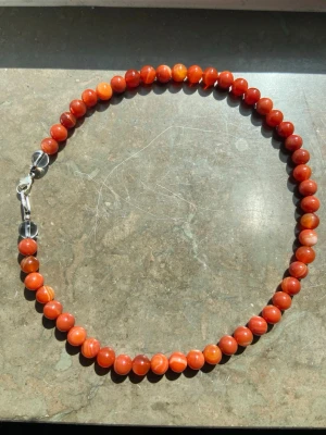 Halsband med äkta agat pärlor  - Snyggt halsband med runda, röda pärlor i olika nyanser av orange och rött. Pärlorna är trädda på rad och halsbandet har ett enkelt metallspänne. Perfekt för dig som vill addera lite färg till din stil.