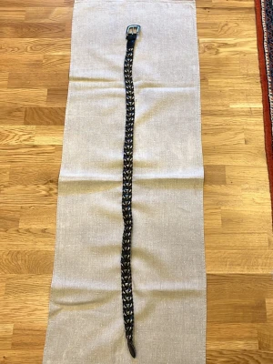 Flätat svart bälte i skinn 110cm - Snyggt flätat svart bälte i skinn med klassiskt spänne i metall. Perfekt accessoar för att lyfta din outfit och funkar till både jeans och byxor. Enkel att justera tack vare det flätade mönstret.