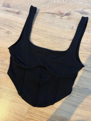 Svart ribbad crop top med breda axelband - Snygg svart crop top i ribbat material med breda axelband och markerad söm under bysten. Toppen har en figurnära passform och en något längre midja som ger en modern siluett. Jätteskönt material, storlek S.🤍