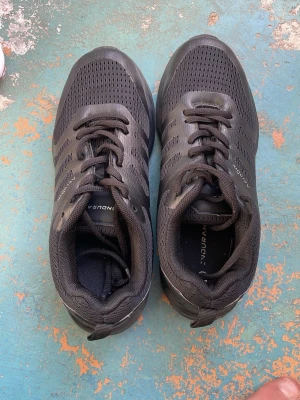 Svarta sneakers från Endurance - Snygga helsvarta sneakers från Endurance med ventilerande mesh-ovandel och klassiska snörningar. Skorna har diskreta ränder på sidorna och en bekväm, vadderad krage. Perfekta för dig som gillar stilrena och sportiga skor.