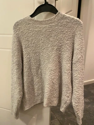 Ljusgrå fluffig stickad tröja - Supermjuk och fluffig ljusgrå stickad tröja från MNG. Tröjan har rund halsringning, lång ärm och en mysig struktur som känns riktigt skön mot huden. Perfekt för kyliga dagar när du vill vara både bekväm och snygg.