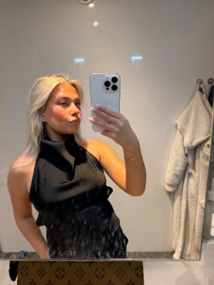 Svart halterneck topp med öppen rygg - Säljer en svart halterneck topp med hög krage och öppen rygg. Toppen har en stilren och elegant look med slät yta och smala band i ryggen. Perfekt för dig som vill ha en trendig och snygg topp till din outfit.