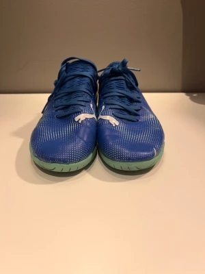 Blåa Puma fotbollsskor inomhus Neymar edition  - Säljer ett par blåa fotbollsskor från Puma med vita detaljer och ljusgröna sulor. Skorna har snörning och är designade för inomhusspel. Ovandelen är i syntetmaterial med ett modernt mönster och stor Puma-logga på sidan.