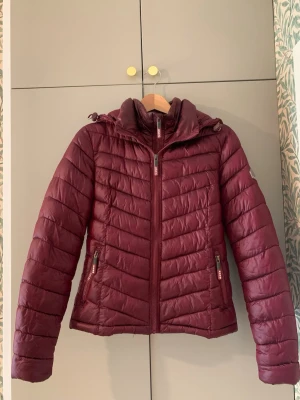 Vinröd jacka Superdry - En vinröd täckjacka från Superdry. Den är i jättefint skick och knappt använd. Den har dock ett litet hål vid hängaren som gått av men ingenting som syns (bild 3). Storlek S. 
