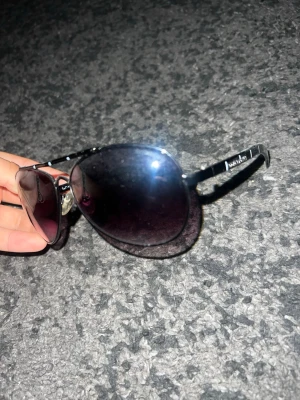 Svarta aviator solglasögon Dolce & Gabbana - Snygga svarta aviator solglasögon från Dolce & Gabbana med metallbågar och mörka tonade glas. Klassisk design med tunna skalmar och diskret logga på sidan. Perfekta för att höja din stil till nästa nivå.