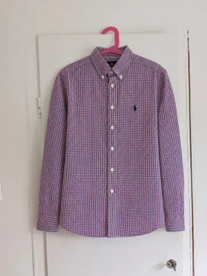 Polo Ralph Lauren rutig skjorta ❤️💙 - Klassisk skjorta från Polo Ralph Lauren med smått rutmönster i rött, blått och vitt. Button-down-krage och den ikoniska broderade Ralph Lauren-loggan på bröstet. Väldigt lättstylad och passar perfekt till jeans, chinos eller under en stickad tröja för en preppy/old money-look. Storlek: M (10-12) Skick: Mycket bra skick, inga defekter!😁 Skriv gärna vid frågor eller om du vill ha mått!