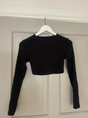 Svart croppad långärmad topp - Snygg svart croppad topp med långa ärmar och rund hals. Perfekt att matcha med höga jeans eller kjol för en trendig look. Enkel och stilren design som passar till många outfits.
