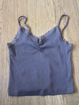 Brunt ribbat linne från Bik Bok - Supersöt brunt ribbat linne från Bik Bok med spetsdetaljer vid urringningen och tunna axelband. Toppen har en liten rynkning framtill och är croppad i modellen. Perfekt att styla med jeans eller kjol!