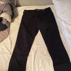 Svarta Replay jeans - Storlek 29/32. Svarta jeans från Replay med klassisk femficksdesign och diskret broderad logga på bakfickan. Byxorna har rak passform och är tillverkade i ett mjukt bomullsmaterial med lite stretch för extra komfort. Perfekta för dig som gillar stilrena och tidlösa jeans.