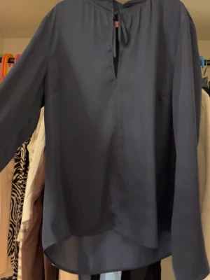 Mörkblå blus från Lawrence Grey - Snygg mörkblå blus från Lawrence Grey med lång ärm och knytband vid halsen. Blusen har en avslappnad passform och är tillverkad i ett glansigt, mjukt material som ger en elegant look. Perfekt att styla med jeans eller kjol.