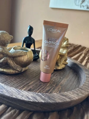 L'Oréal LUMI Glotion 903  - LUMI Glotion Natural Glow Enhancer från L'Oréal Paris i nyansen 903. Tuben är brun med roséguldfärgat lock och text i vitt. Produkten ger en naturlig glow och kan användas som foundation eller highlighter för en fräsch look.