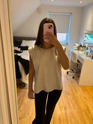 Beige ärmlös linnetopp med axelvaddar - Snygg beige linnetopp med markerade axelvaddar och rund halsringning. Toppen har en loose passform och är perfekt för en trendig och avslappnad look. Materialet känns mjukt och lätt mot huden.