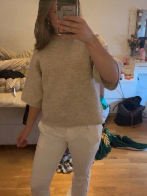 Beige stickad tröja med halvlånga ärmar - Säljer en beige stickad tröja med halvlånga, vida ärmar och rak passform. Tröjan har en enkel och stilren design, perfekt att matcha med olika outfits. Materialet är mjukt och bekvämt ut, och färgen är lätt att bära till det mesta. Använd ungefär 2 gånger.
