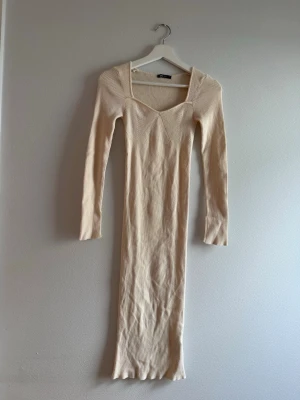 Beige ribbad långklänning - Långklänning i beige med ribbad struktur och lång ärm. Klänningen har en fyrkantig ringning och är figurnära i modellen. Perfekt för dig som gillar stilrena och enkla plagg med en modern touch. Från H&M.
