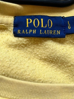 Gul sweatshirt Polo Ralph Lauren - Gul sweatshirt från Polo Ralph Lauren med ikoniska Polo Bear-trycket på bröstet. Tröjan har rund halsringning, långa ärmar och ribbade muddar. Tillverkad i mjukt bomullsmaterial för en skön och avslappnad look.