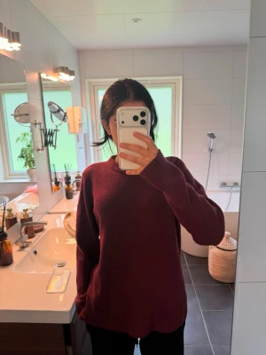 Vinröd oversized stickad tröja - Mysig vinröd stickad tröja med avslappnad passform och rund hals. Tröjan har långa ärmar och ribbade muddar vid ärmslut och nederkant. Perfekt för lager på lager och höstmys.