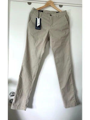 Mason’s - helt NYA beiga byxor / chinos - storlek XS / 44 - Helt nya beiga byxor/ chinos från Mason's i storlek 44 / XS (herr). Klassisk design med raka ben, knappstängning och praktiska fickor fram och bak. Finvävt material i 97% bomull och 3% elastan, så bra material som både andas och har lite stretch för bra passform. En stilren och mångsidig byxa som passar för många tillfällen. Nypris 1950:-. HELT NYA med etikett!