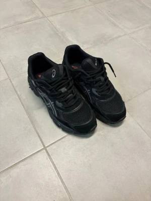 Svarta Asics gel nyc storlek 45 - Säljer ett par svarta Asics sneakers med coola meshpaneler och reflekterande detaljer på sidorna. Skorna har en chunky sula och klassisk snörning. Perfekta för dig som gillar sportig och stilren look.