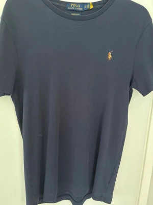 Mörkblå t-shirt från Polo Ralph Lauren - Snygg mörkblå t-shirt från Polo Ralph Lauren med klassisk broderad logga på bröstet. T-shirten har rund halsringning och korta ärmar. Tillverkad i mjuk bomull för skön känsla hela dagen.