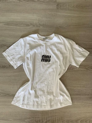 Vit Miu Miu t-shirt med zebra-tryck - Säljer en vit t-shirt från Miu Miu med ett coolt zebramönstrat tryck på bröstet. Klassisk passform med rund hals och korta ärmar. Perfekt för dig som gillar stilrena plagg med en twist.