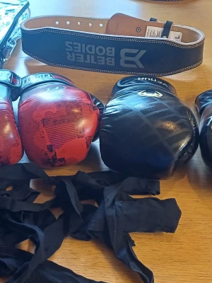 Boxningshandskar och träningsbälte - Säljer ett set med svarta boxningshandskar från Venum, röda boxningshandskar, ett svart träningsbälte från Better Bodies och svarta lindor. Perfekt för boxning eller kampsportsträning. Handskarna har klassisk form och kardborrestängning.