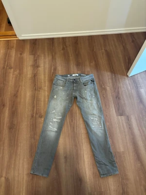 Gråa Replay Anbass jeans herr - Replay Anbass jeans – W34 L32 👖 Snygga grå/svart tvättade jeans från Replay i modellen Anbass. Slim fit med snyggt slitna detaljer och washed look. Jeansen är i storlek W34/L32 och är gjorda i ekologisk bomull.