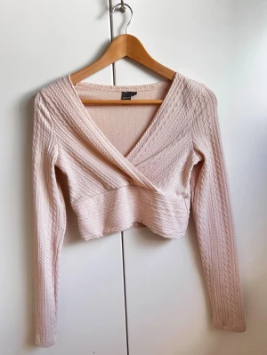 Ljusrosa/Beige omlottopp med v-ringning - Långärmad crop top med omlottdesign framtill. Nyskick, knappt använd. Toppen har en texturerad yta och en figurnära passform i Stl. S från Shein