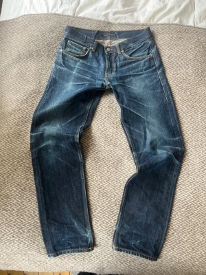 Nudie gritty jackson dry selvage - Saljer nu mina Gritty Jackson selvedge jeans från Nudie. Använda i 6 månader med en tvätt vilket har resulterat i dessa fina fades som det bara är att bygga vidare på. Har blivit hål i fickorna från min mobil men går enkelt att lämna in på Nudies butik för gratis lagning. Storleken är 32/32 men efter tvätten skulle jag säga att de sitter perfekt som 31/32.  Midja: 42cm Innerben:  79cm Ytterben: 106cm Benöppning: 19cm