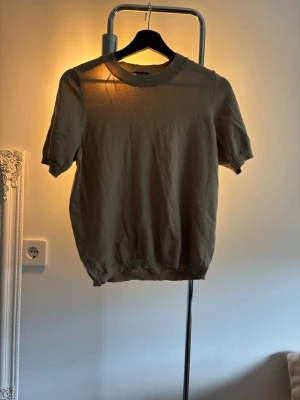 Väldigt ljus brun stickad topp från Lindex - Säljer en ljus brun stickad topp från Lindex med korta ärmar och rund halsringning. Toppen har en ribbad kant vid halsen och är tillverkad i ett mjukt material som passar perfekt till många olika stilar.