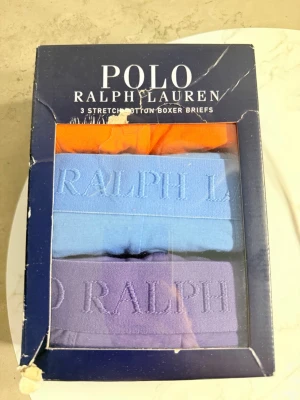 3-pack kalsonger Polo Ralph Lauren XL - Säljer ett 3-pack stretchiga bomullskalsonger från Polo Ralph Lauren i färgerna orange, ljusblå och lila. Kalsongerna har bred resår med broderad logga och är tillverkade i 95% bomull och 5% elastan för skön passform.