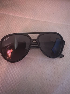 Svarta Ray-Ban aviator solglasögon - Snygga svarta aviator solglasögon från Ray-Ban med mörka glas och klassisk pilotform. Modellen har en cool detalj med öppen brygga och Ray-Ban-logga på linsen. Perfekta för dig som vill ha en tidlös och trendig look.