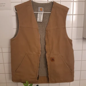 CARHARTT VÄST  - Carhartt väst i beiget/tan med fårskinnsfoder. Mycket varm å snygg. Skulle säga att det är en L men lirw beroende på hur man vill atr den ska sitta men vädigt stor på mig som är 165 å rätt liten. Allmänt slitage men inga märken eller så