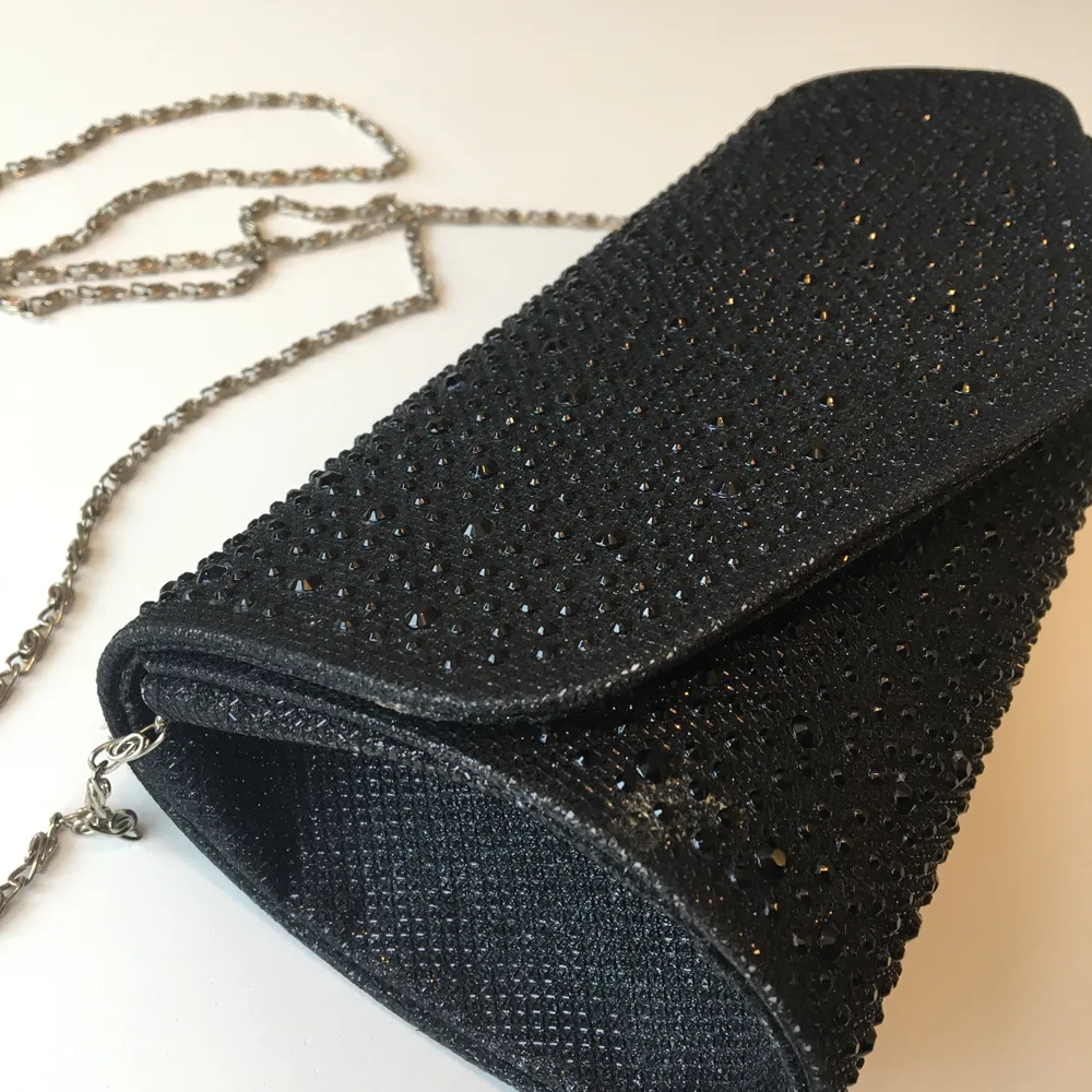 Snygg, svart, glittrig partyväska i hårt material. Stängs med magnetknapp, avtagbar kedja, litet fack på insidan.. Väskor.