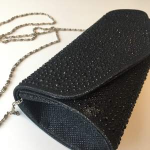 Snygg, svart, glittrig partyväska i hårt material. Stängs med magnetknapp, avtagbar kedja, litet fack på insidan.