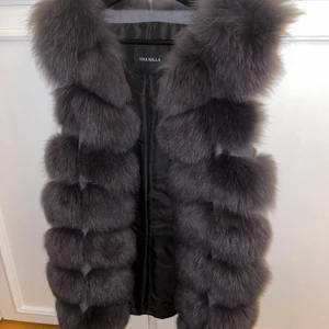 VivaNilla pälsväst (äkta) - Mörkgrå pälsväst från Vivanilla. Använd max 3 gånger så absolut nyskick. Det är fin äkta päls med mocka/skinn mellan pälsraderna. Går att ha både vår, sommar och höst då den är tjock, kan ha en tunnare jacka under. Går även att knäppa. Köpt på vivanilla